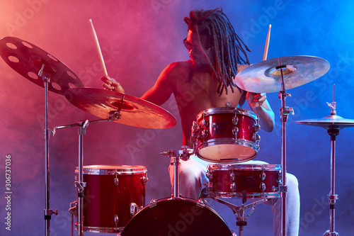 Fototapeta portrait of african man with naked skin, wearing eyeglasses sit playing on drums