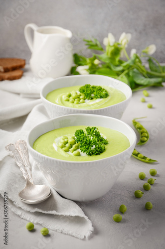 Green pea soup in bowls on gray concrete or stone background.