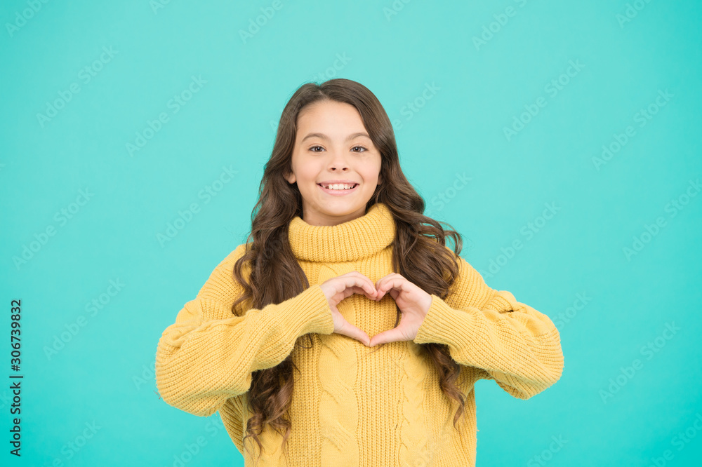 Happy child feel warm and cozy. child in casual winter fashion style. happy childhood. Small girl long hair show heart. love in her heart. knitting for kids. Little girl on blue background Happy child feel warm and cozy. child in casual winter fashion style. happy childhood. Small girl long hair show heart. love in her heart. knitting for kids. Little girl on blue background
