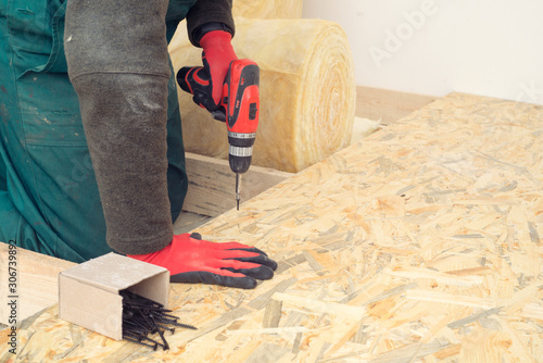 Fotografia Man worker screws wooden oriented stands bords on insulated floor