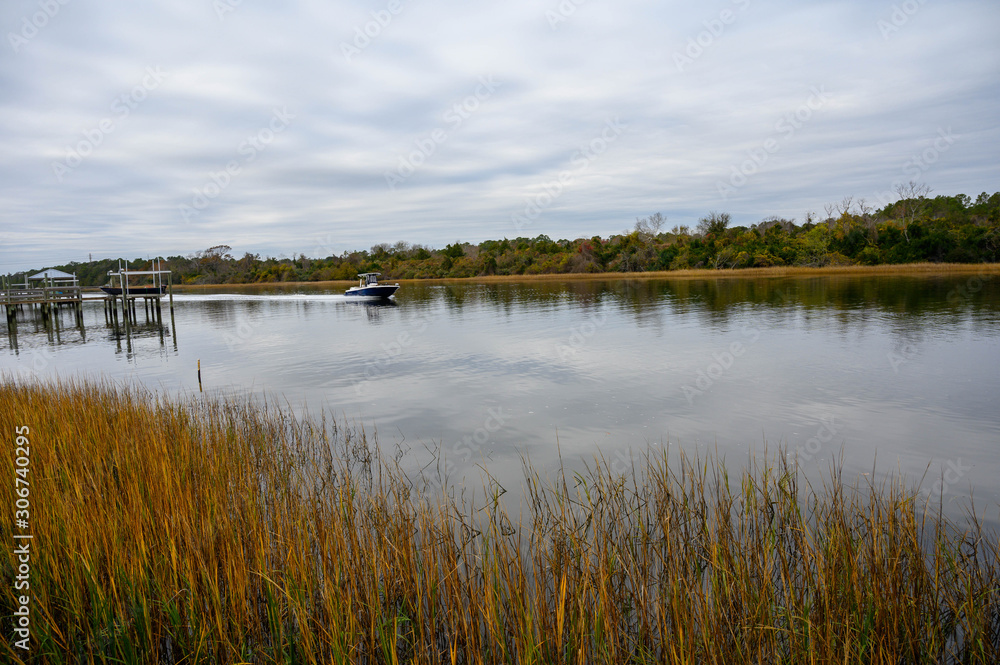 A boat is speeding down the waterway. The calm water is surrounded by grass in the waterway.