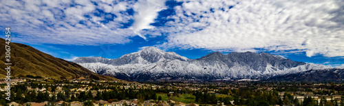 Aerial panorama of snow covered San Gorgonio and Little San Bernardino Mountains on a winter day above Yucaipa Valley with blue sky, white clouds, houses, hills
