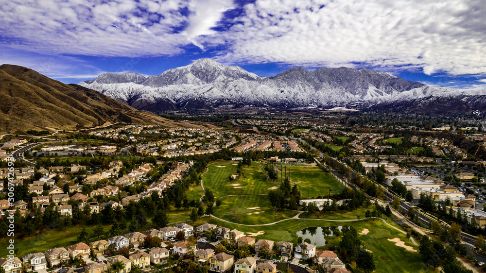 Aerial panorama of snow covered San Gorgonio and Little San Bernardino Mountains on a winter day above Yucaipa Valley with blue sky, white clouds, houses, hills
