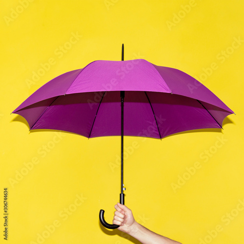A man holds in his hand a purple umbrella on a background of yellow lime wall. Concept autumn, business, art.