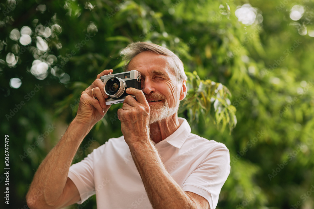 Senior man making photographs on film camera while walking outdoors Senior man making photographs on film camera while walking outdoors