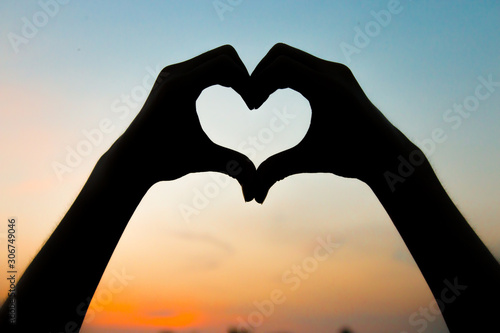 Silhouette hand in heart shape on sunrise with sky