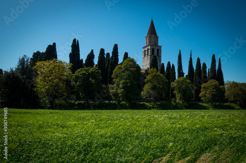 Tower of Basilica di Aquileia in Italy with meadows, trees, cypress and clear blue sky