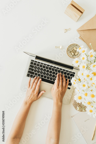 Women's hands work composition. Home office desk workspace with laptop, chamomile daisy flowers bouquet and notebook on white background. Flat lay, top view copy space mockup.
