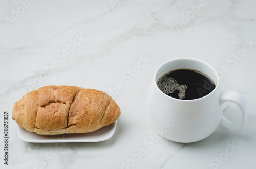 White mug with black coffee and croissant on white stone table. Coffee break.