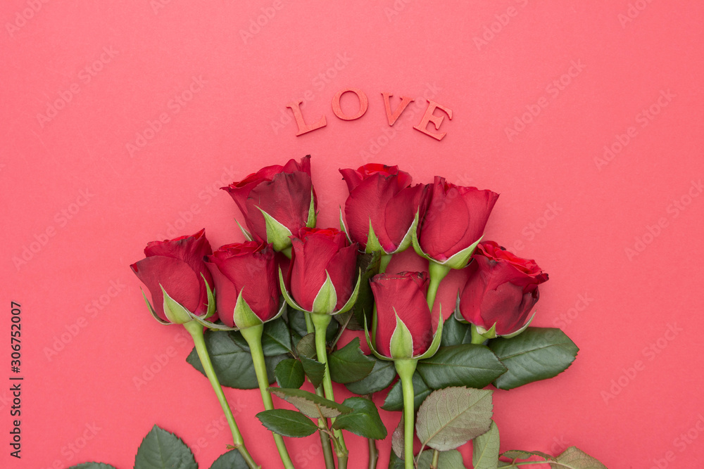 Fototapeta premium Red roses and LOVE letters inscription, over pink background flat lay. Valentine's Day, Birthday abstract background with copy space.