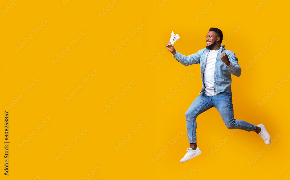 Black man jumping with money in hand, excited about big sales