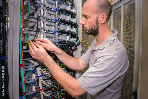 The system administrator works in the data center. Portrait of a technician working with computer equipment. Network engineer switches power cables in the server room rack