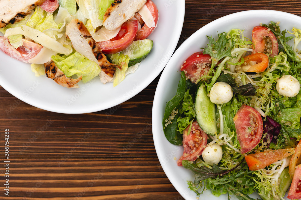 white deep plates with fresh salad ingredients mixed with sauce placed on a rustic background. A place for a menu, banner or advertisement