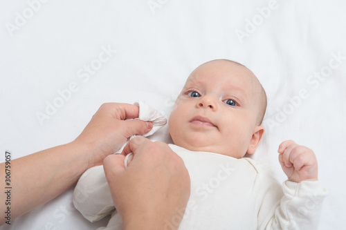 Mother hand cleaning baby ear and nose with a cotton swab. Baby taking care and hygiene concept.