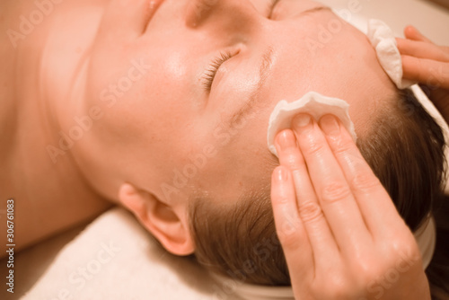 plus size relaxed woman lying in the spa salon and get cleaning skin with cotton pads