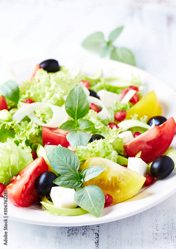 Salad with black Olives, red and yellow Tomatoes, Feta Cheese and Pommegranate Seeds on bright wooden Background. Healthy Snack Idea. Close up. Salad with black Olives, red and yellow Tomatoes, Feta Cheese and Pommegranate Seeds on bright wooden Background. Healthy Snack Idea. Close up.