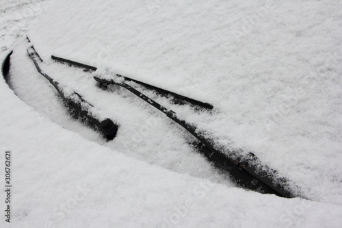 Car front side with snowy windshield glass in winter - driving safety, close up front view to screen wiper photo