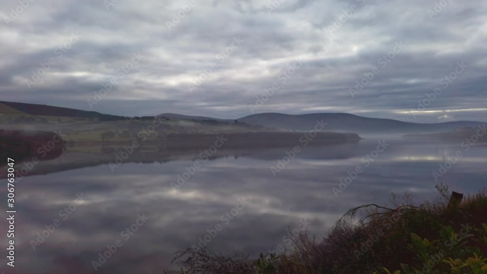 scenic wide pan shot of Blessington Lake Ireland in mystical twilight of cloudy sky reflecting in calm smooth glassy water surface and fog shorelines mountains and forest. Creepy vegetation no people scenic wide pan shot of Blessington Lake Ireland in mystical twilight of cloudy sky reflecting in calm smooth glassy water surface and fog shorelines mountains and forest. Creepy vegetation no people