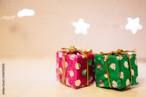 Two small gift boxes wrapped in festive Christmas paper lie on the table, and a garland of lights in the shape of stars photo