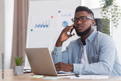 Foto Afro manager talking on phone at workplace with concerned face expression