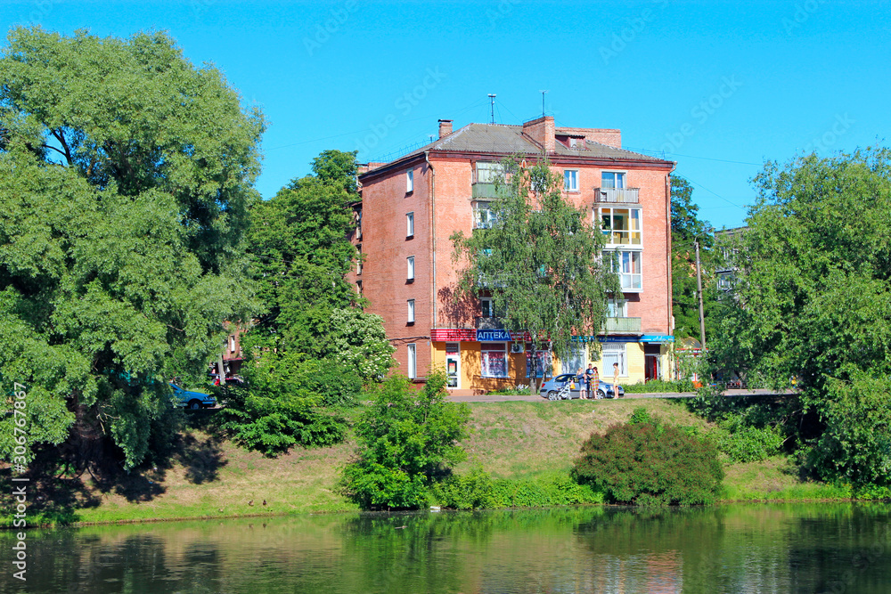 Multi-storey house standing in green trees near river. Nature in city