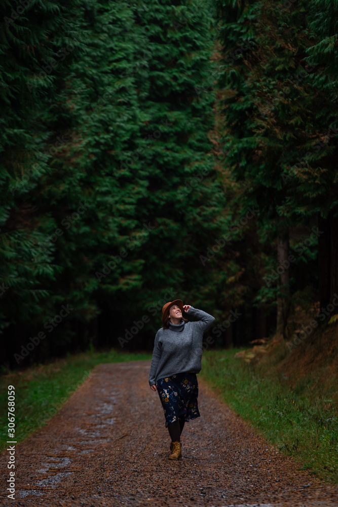 beautiful young woman with hat, sweater and skirt walking on a pine forest path. Otzarreta, Basque Country, Spain