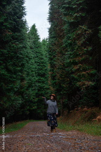 beautiful young woman with hat, sweater and skirt walking on a pine forest path. Otzarreta, Basque Country, Spain