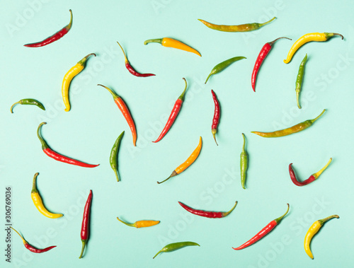 Red, green and yellow hot chili peppers in flat lay style texture. Pattern on neon mint background.