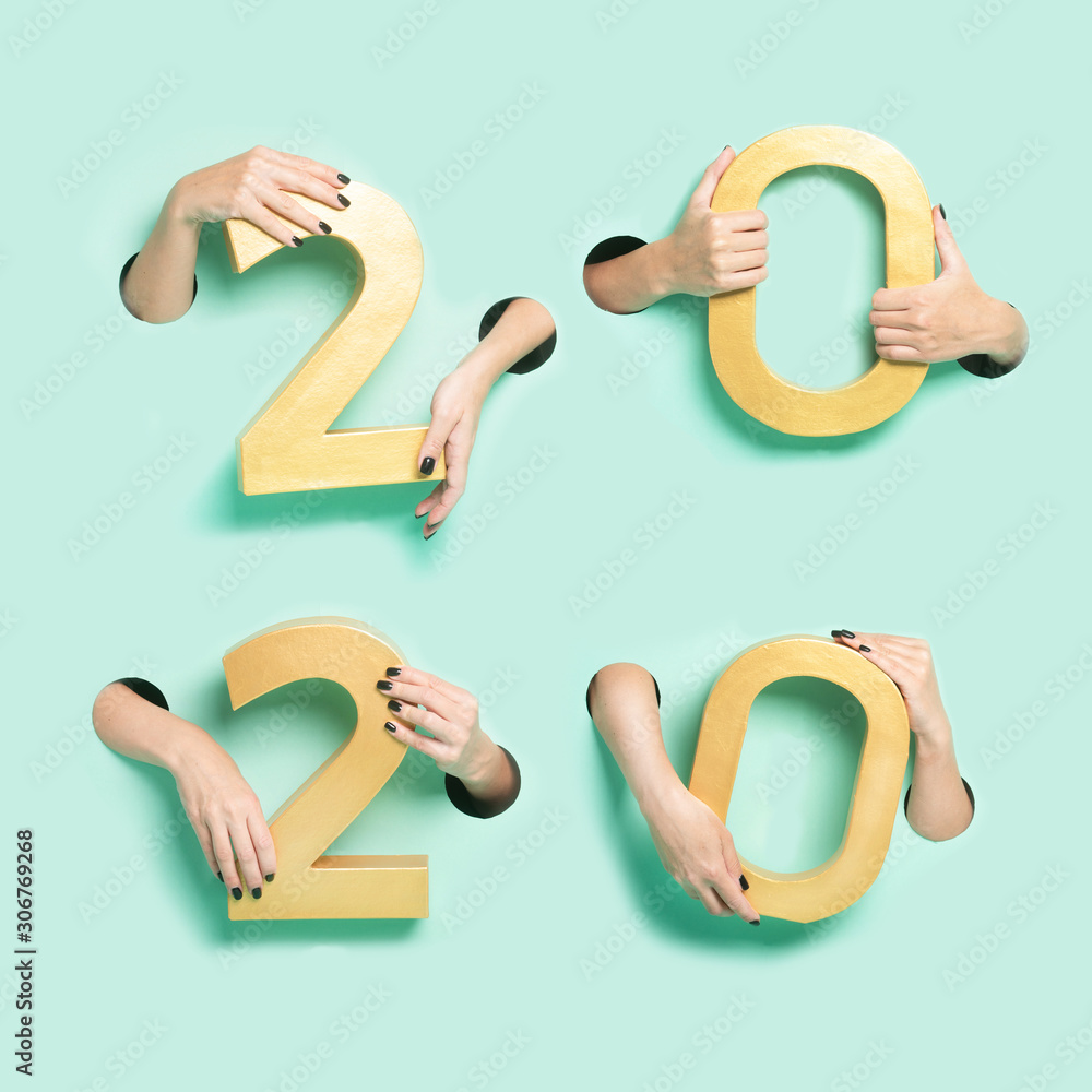 Female hands hold golden new year 2020 digits through a hole on neon mint background. Female hands hold golden new year 2020 digits through a hole on neon mint background.