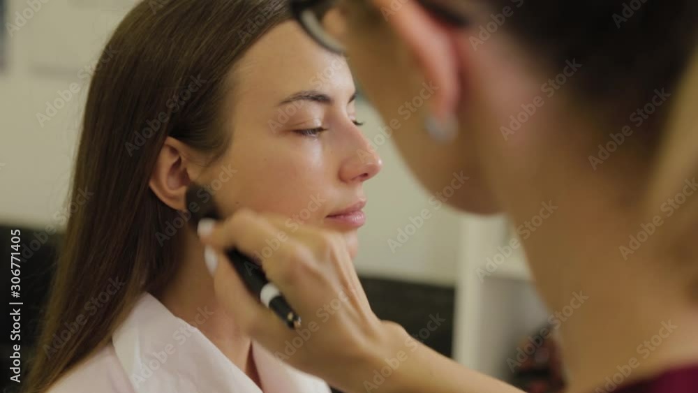 Professional make-up artist applies foundation cream on client's face with brush. Professional make-up artist applies foundation cream on client's face with brush.