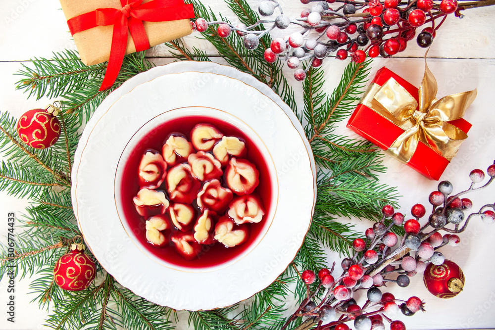 Traditional Polish Christmas Eve dish - red borscht with dumplings, spruce branches, gifts and red baubles in the background Traditional Polish Christmas Eve dish - red borscht with dumplings, spruce branches, gifts and red baubles in the background