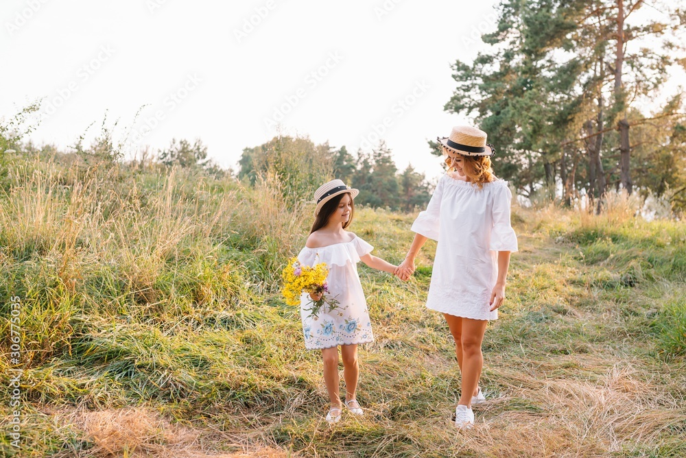Fototapeta premium Cheerful mother and her little daughter having fun together in the summer background. Happy family in the nature background. Cute girls with colorful flowers.