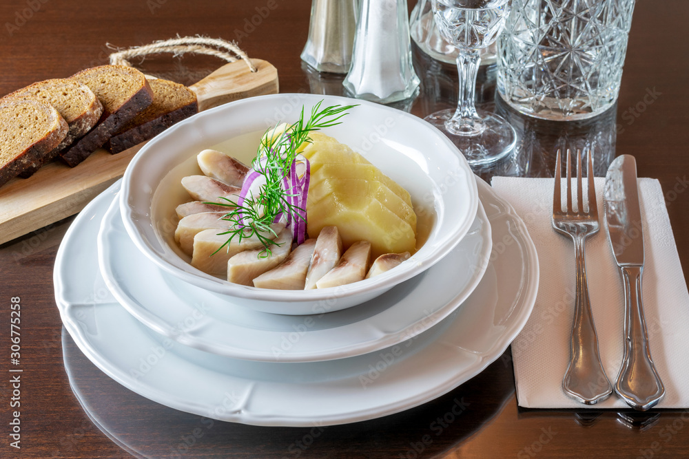 Restaurant menu. White plate with slices of salted herring and boiled potato, decorated with cut onion and dill. Restaurant menu. White plate with slices of salted herring and boiled potato, decorated with cut onion and dill.