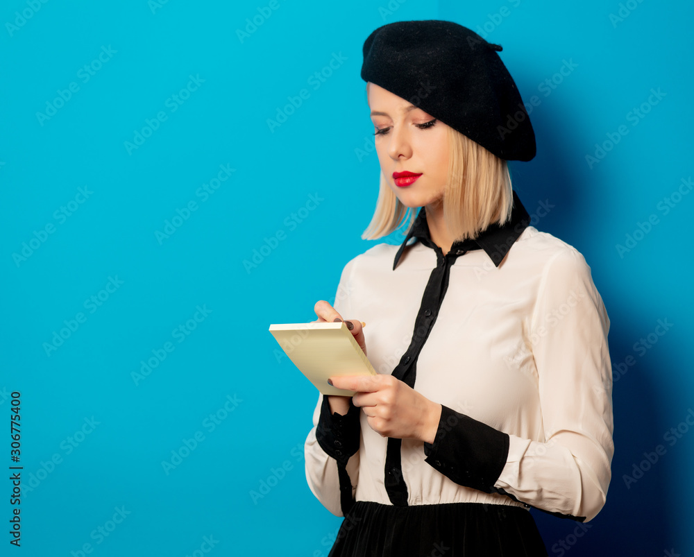 © Masson - beautiful french woman in beret holds notebook with pencil on blue background © Masson - beautiful french woman in beret holds notebook with pencil on blue background
