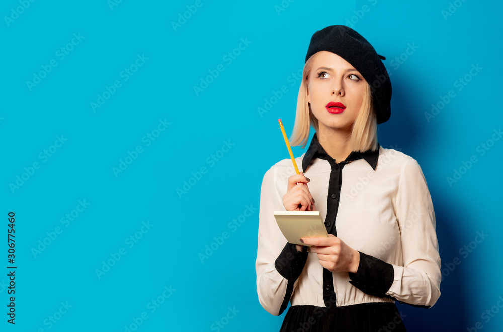 beautiful french woman in beret holds notebook with pencil on blue background beautiful french woman in beret holds notebook with pencil on blue background