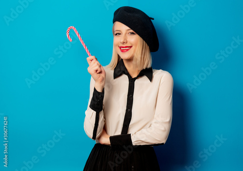 beautiful french woman in beret with lollipop candy on blue background