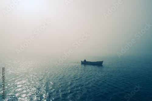 Fishing boat and fisherman in the sea, foggy morning over the water © ValentinValkov