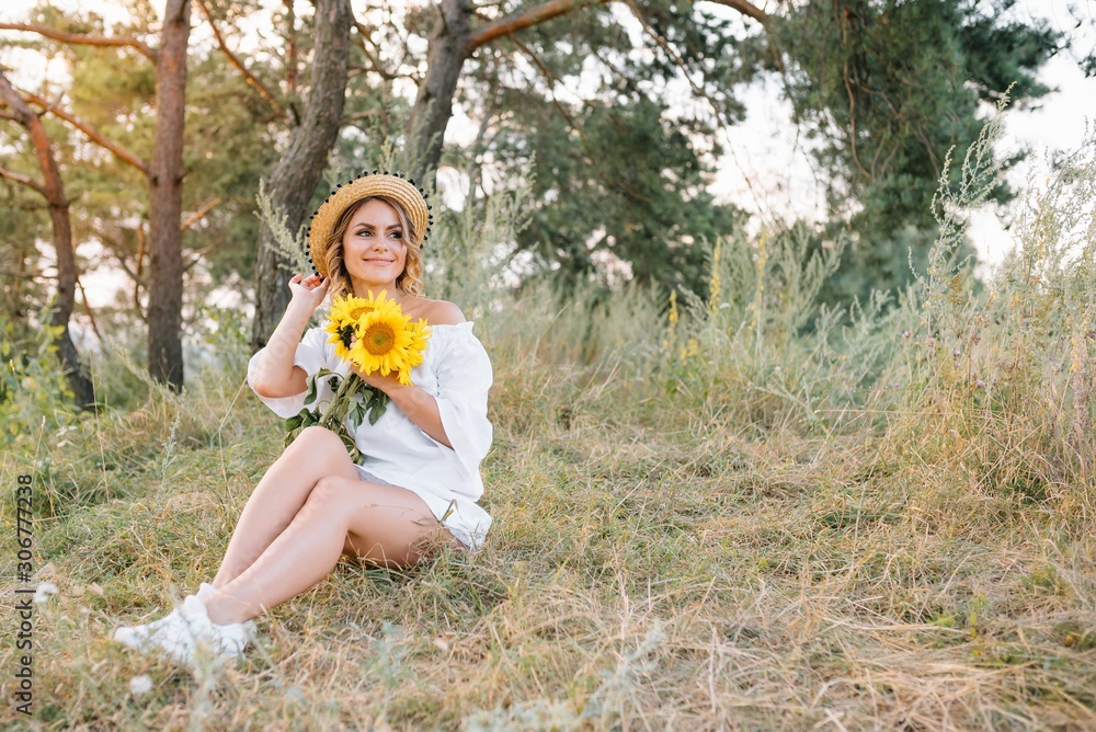 Outdoor shot of pleasant looking female with tanned healthy skin, dressed in white dress and summer hat, poses in park with confident satisfied expression, likes recreation. Beautiful young woman Outdoor shot of pleasant looking female with tanned healthy skin, dressed in white dress and summer hat, poses in park with confident satisfied expression, likes recreation. Beautiful young woman
