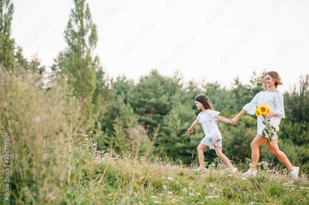 Cheerful mother and her little daughter having fun together in the summer background. Happy family in the nature background. Cute girls with colorful flowers.