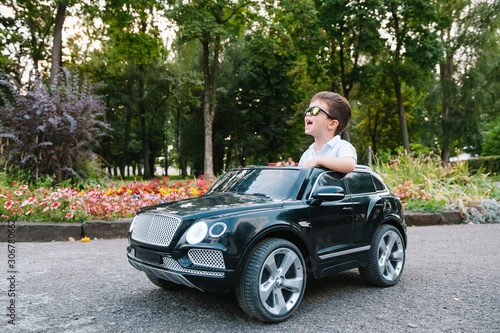 Cute boy in riding a black electric car in the park. Funny boy rides on a toy electric car. Copy space.