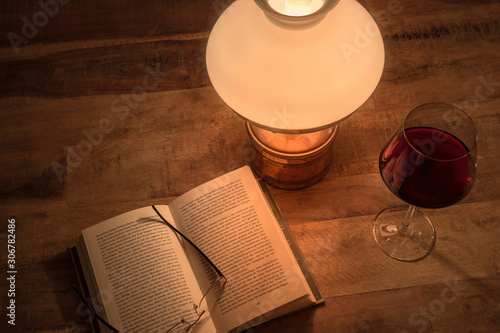 Old table lamp with book and glass of red wine on old wooden table