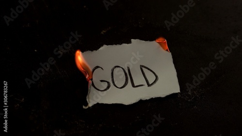 Gold word written on white paper burns. Fire with smoke and ashes on black background photo