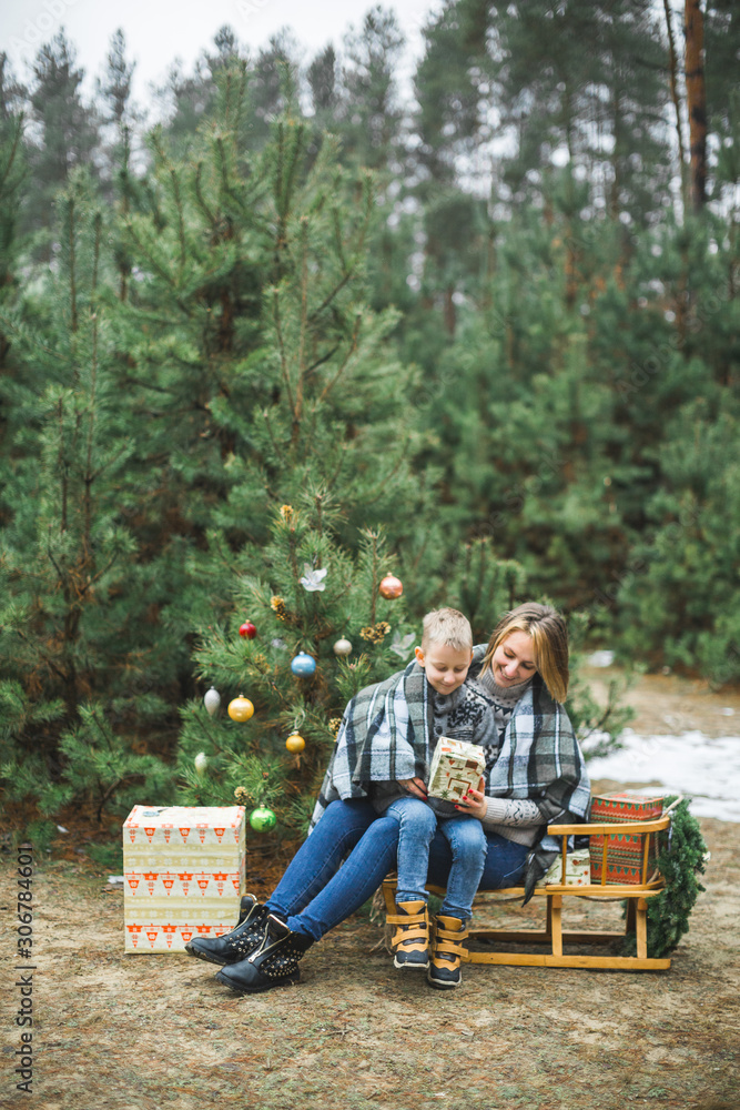 © sofiko14 - Mother and son in gray knitted sweaters enjoying beautiful winter day outdoors, while sitting on wooden sledge decorated with nice Christmas Santa presents. Decorated Christmas tree © sofiko14 - Mother and son in gray knitted sweaters enjoying beautiful winter day outdoors, while sitting on wooden sledge decorated with nice Christmas Santa presents. Decorated Christmas tree