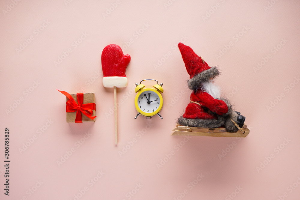 Christmas flat lay composition. Yellow alarm clock, gift, candy and Santa Claus in a sleigh on a beige background.