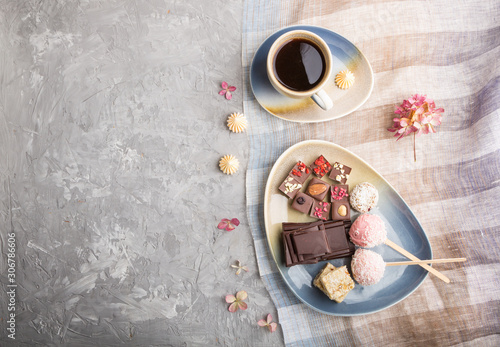 A pieces of homemade chocolate with coconut candies and a cup of coffee on a gray concrete background. top view, copy space.