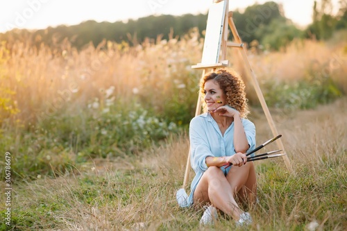 Pretty woman is painting. Open air session. Cute woman draws a picture at sunset. girl artist © Serhii