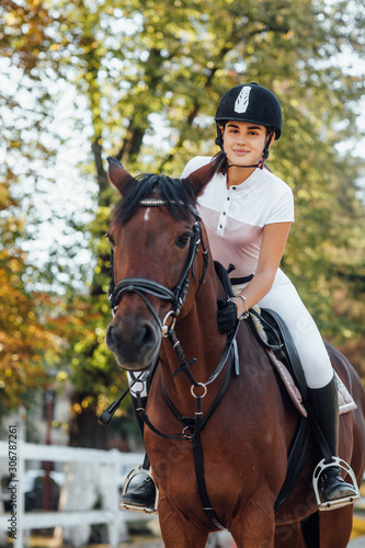 Young jockey girl riding a brown horse in autumn forest.