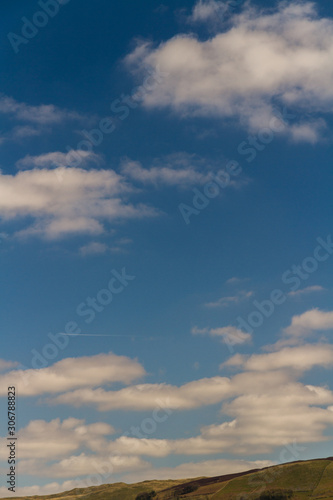 Clouds in clue sky, green hill at bottom.