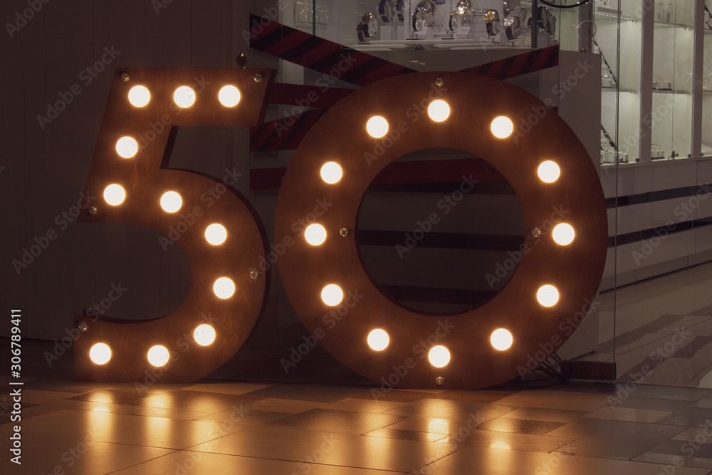 number 50 carved from wood with bright bulbs around the perimeter. The concept of discounts and sales in stores, an important date - anniversary, anniversary, birthday - obrazy, fototapety, plakaty 