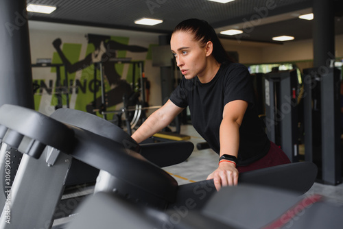 Portrait of a woman resting after her workout. She is leaning on a treadmill and looks completely exhuasted.